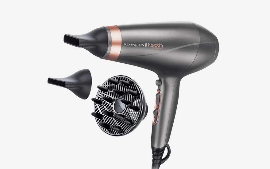 Grijze Remington haardroger met koperkleurige accenten ligt naast twee smalle mondstukken en een ronde diffuser met opvallende pinnen.