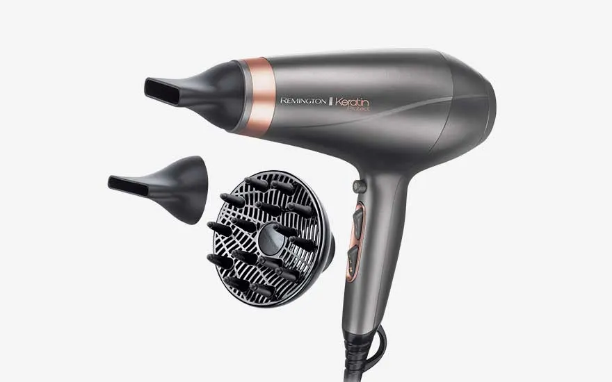 Grijze Remington haardroger met koperkleurige accenten ligt naast twee smalle mondstukken en een ronde diffuser met opvallende pinnen.