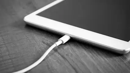 Een witte kabel is aangesloten op een witte tablet op een houten oppervlak.