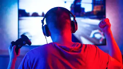 Man met koptelefoon speelt videospel met controller voor een tv-scherm en balt een vuist.
