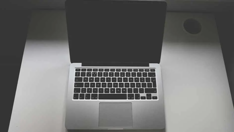 Een opengeklapte laptop staat op een wit bureau. Het scherm is zwart en het toetsenbord is zilverkleurig met zwarte toetsen.