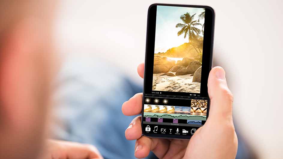 Een hand houdt een smartphone met een video-editor app open, waarop een strandscène met een palmboom te zien is.