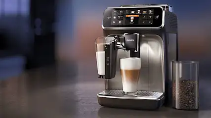 Een Philips koffiemachine met een glas melk en een glas latte macchiato, naast een pot met koffiebonen.