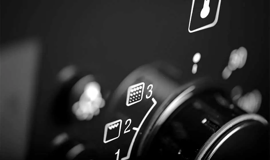 A close-up shows the control knob of an oven or cooker, with settings and symbols clear on a glossy black panel.