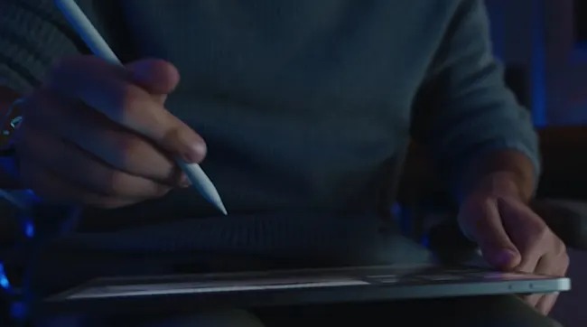 Een persoon tekent op een tablet met een witte styluspen in een donkere omgeving.