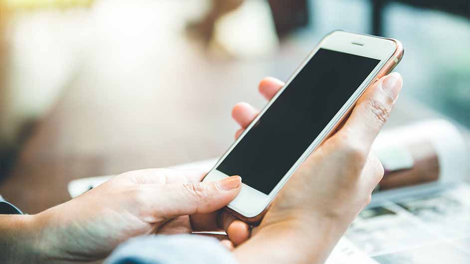 Een persoon houdt een smartphone met een zwart scherm vast. De achtergrond is wazig.