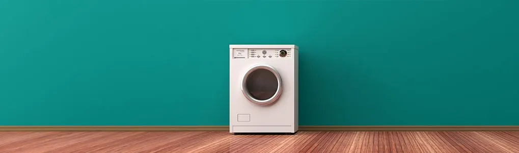 A front-facing view of a white front-load washing machine is set against a teal wall and wood floor.