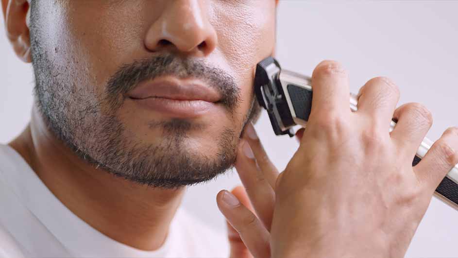 Een man gebruikt een elektrisch scheerapparaat bij zijn baard, met een witte achtergrond.