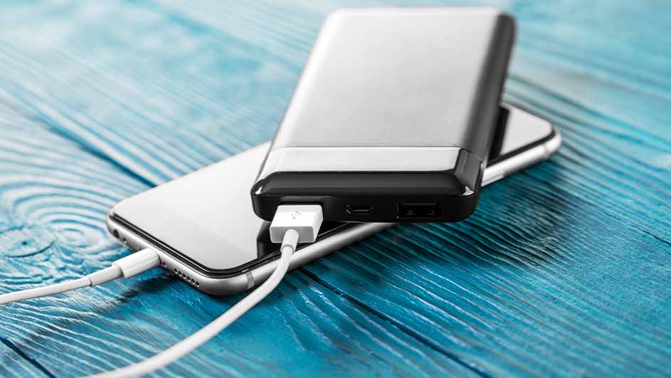 Een telefoon wordt opgeladen door een powerbank op een blauwe houten tafel met een witte kabel.