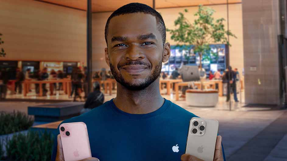 Een man in een blauw shirt houdt een roze en een witte iPhone vast in een winkel met houten tafels en planten.