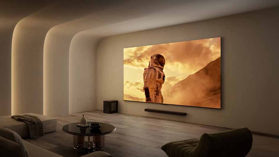 Woonkamer met een groot scherm met een astronaut, een zwarte soundbar, een tafel en een bank.