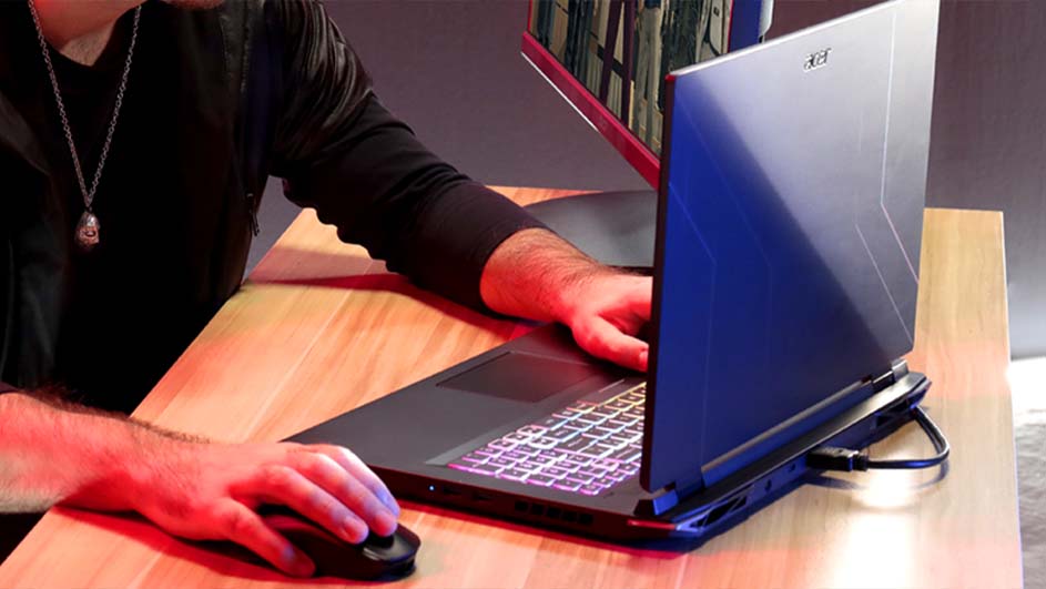 Een persoon gebruikt een laptop en muis op een houten bureau, met een tweede scherm zichtbaar op de achtergrond.