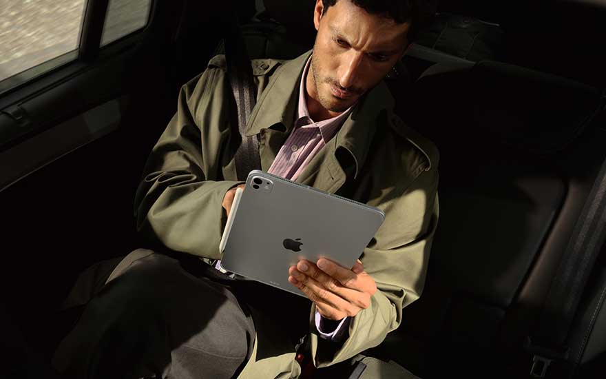 Man in auto op achterbank gebruikt een zilveren tablet met beide handen, verdiept in werk of media tijdens de rit.