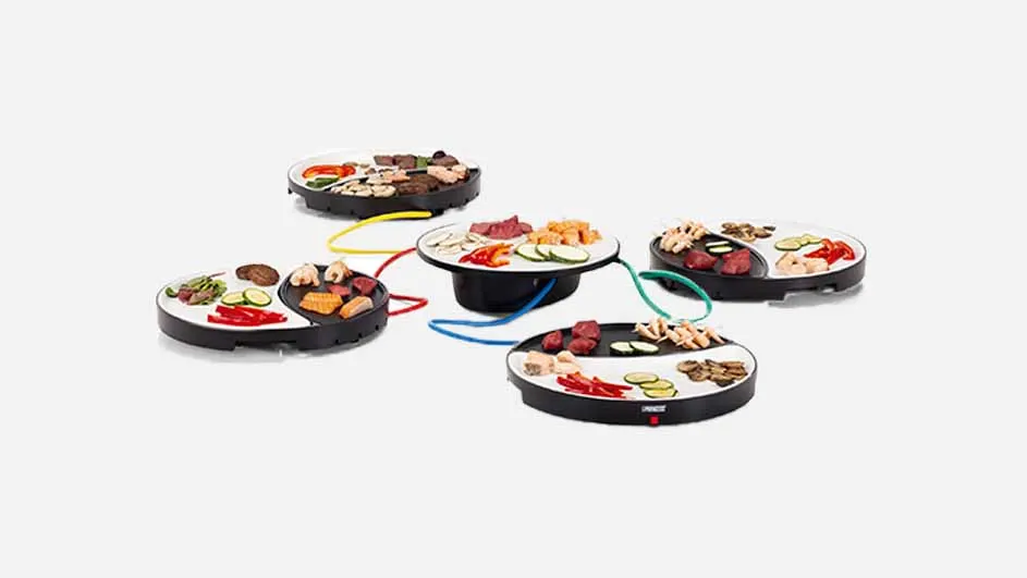 Vijf ronde, zwarte kookplaten met kleurrijke snoeren, elk met een witte helft vol gesneden groenten en vlees.