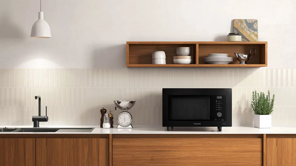 Een keuken met houten kasten, een zwarte magnetron, een wasbak, een open houten wandkast en een witte lamp.