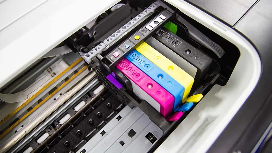 Binnenkant van een printer met zwarte, magenta, blauwe en gele inktcartridges. Metalen geleiders en plastic onderdelen zijn zichtbaar.