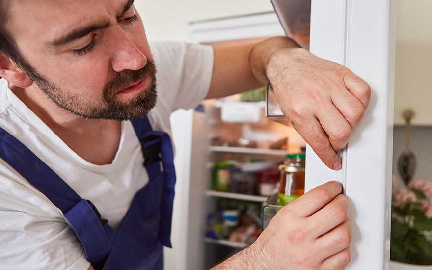 Technicus in overall inspecteert zorgvuldig de koelkastdeur, let op het rubberen afdichtingsprofiel voor goed functioneren.