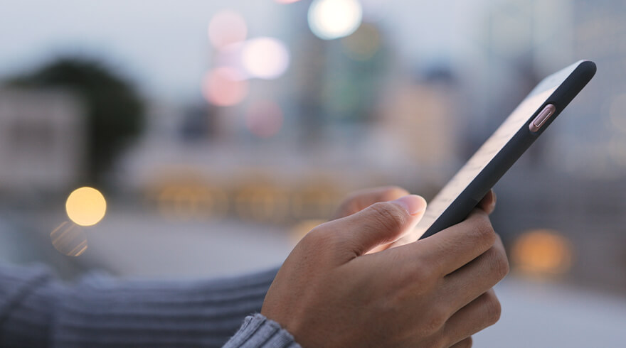 Handen houden een verlichte tablet vast, met gebouwen en bokeh-lichten op de achtergrond.