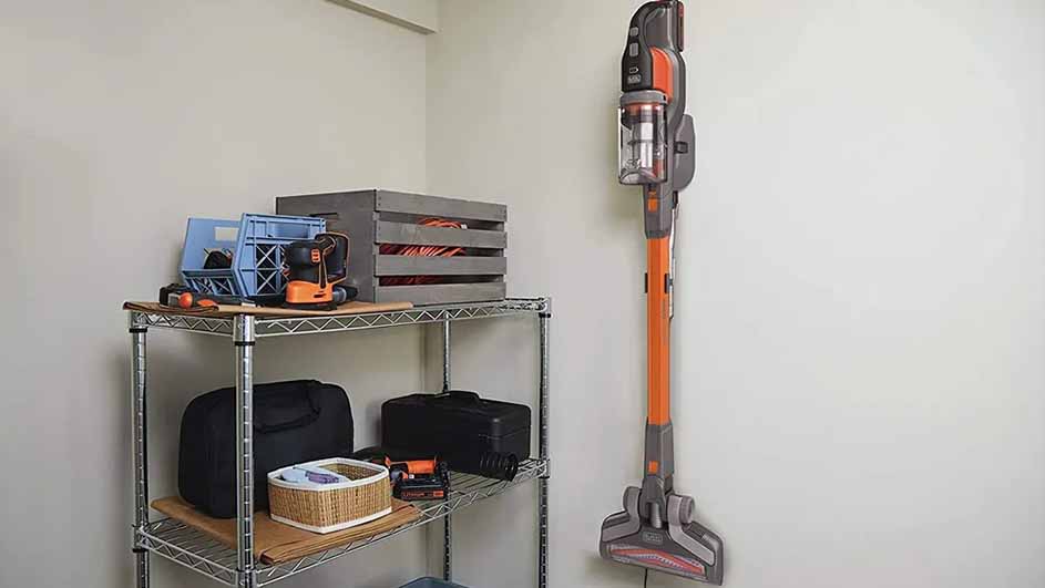 Een kamerhoek met een metalen stellingkast gevuld met opbergbakken, een gereedschapskist en een stofzuiger aan de muur.