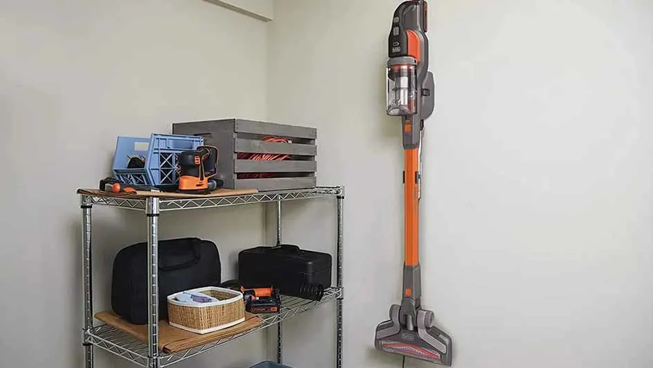 Een kamerhoek met een metalen stellingkast gevuld met opbergbakken, een gereedschapskist en een stofzuiger aan de muur.