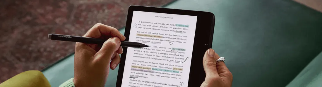 Hands hold a tablet displaying text with highlights, using a stylus for annotation. A ring is visible on a finger.