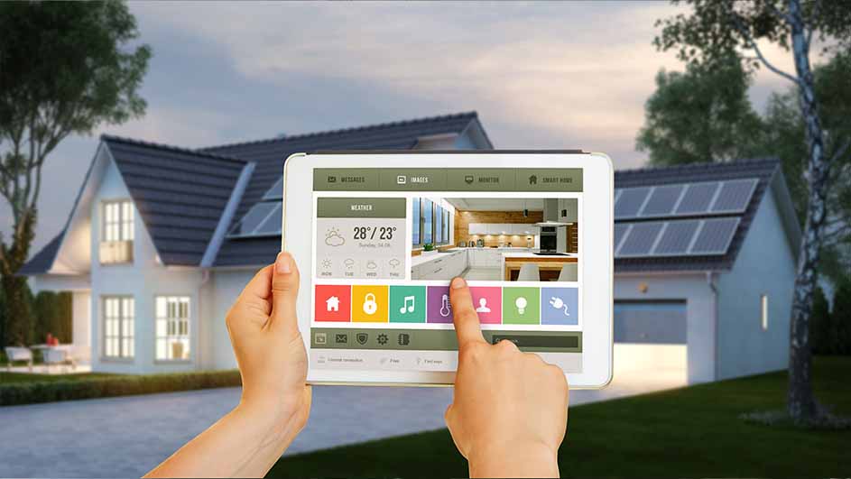 Handen bedienen een tablet met een smart home interface tegen de achtergrond van een huis met zonnepanelen en een tuin.