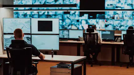 Een controlekamer met mensen achter bureaus die naar meerdere computerschermen kijken.