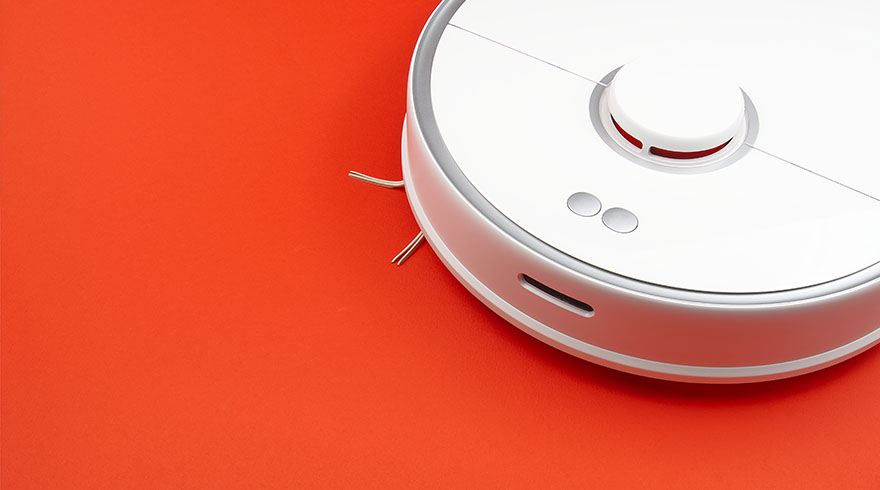 Witte robotstofzuiger met zilveren rand en gouden borstels op een oranje achtergrond.