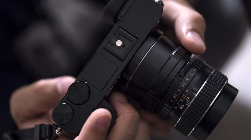 Een zwarte camera met lens wordt door twee handen vastgehouden, scherp gefocust op de details van de lensringen.