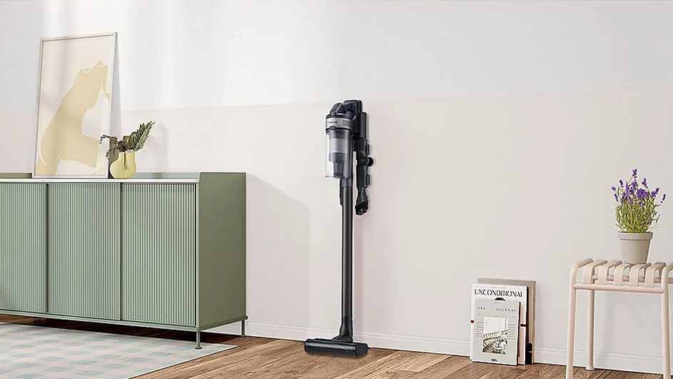 Een woonkamer met een groene kast, een stofzuiger aan de muur, een plant en een tijdschrift op de houten vloer.