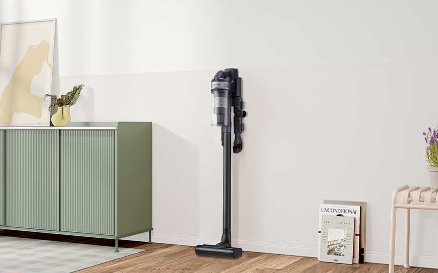 Een donkere steelstofzuiger staat aan de muur in een lichte kamer met groen dressoir, houten vloer, kunst aan de muur en kleine accessoires.