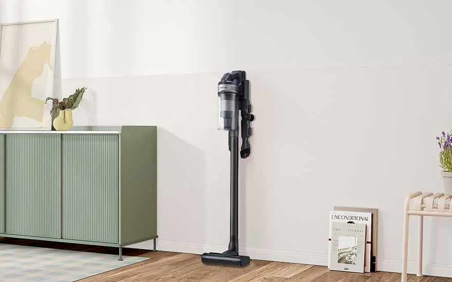 Een donkere steelstofzuiger staat aan de muur in een lichte kamer met groen dressoir, houten vloer, kunst aan de muur en kleine accessoires.