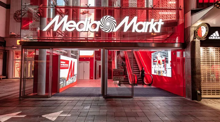 Winkelpui van Media Markt met glazen schuifdeuren, rode accenten en een roltrap zichtbaar binnen.