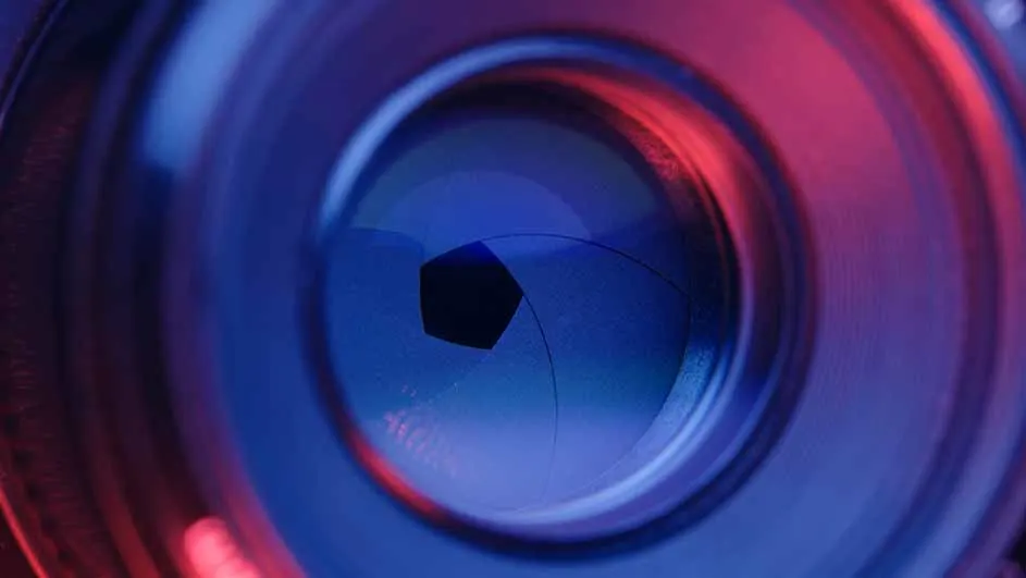 Close-up van een cameralens met een zeshoekige opening, verlicht in blauw en rood.