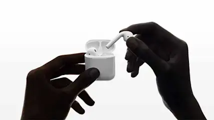 Two hands hold a white case with white wireless earbuds against a white background, one earbud is held separately.