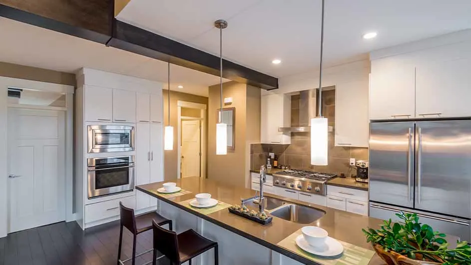 Een keuken met witte kasten, roestvrijstalen apparaten, een eiland met stoelen en hanglampen.