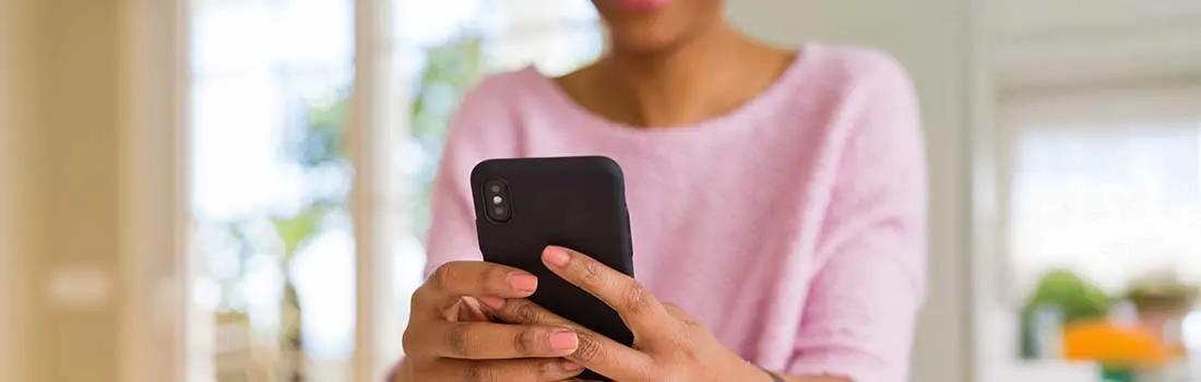 Close-up van een vrouw die binnen, in zacht daglicht, haar smartphone vasthoudt en met haar andere hand op het scherm tikt.