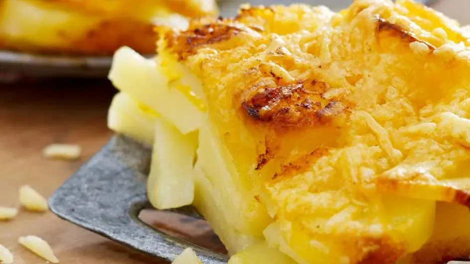 Een close-up van een aardappelgratin met een goudbruine, kaasachtige korst op een grijze spatel.