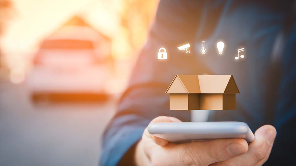 Hand houdt smartphone met huisicoon en slimme huisbedieningssymbolen erboven, op achtergrond een huis.