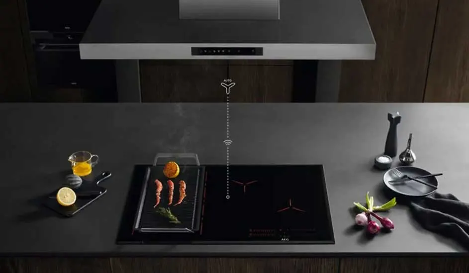 Donkere keuken met AEG-inductiekookplaat, grillplaat met garnalen en groente, zachte verlichting en een strakke afzuigkap erboven.