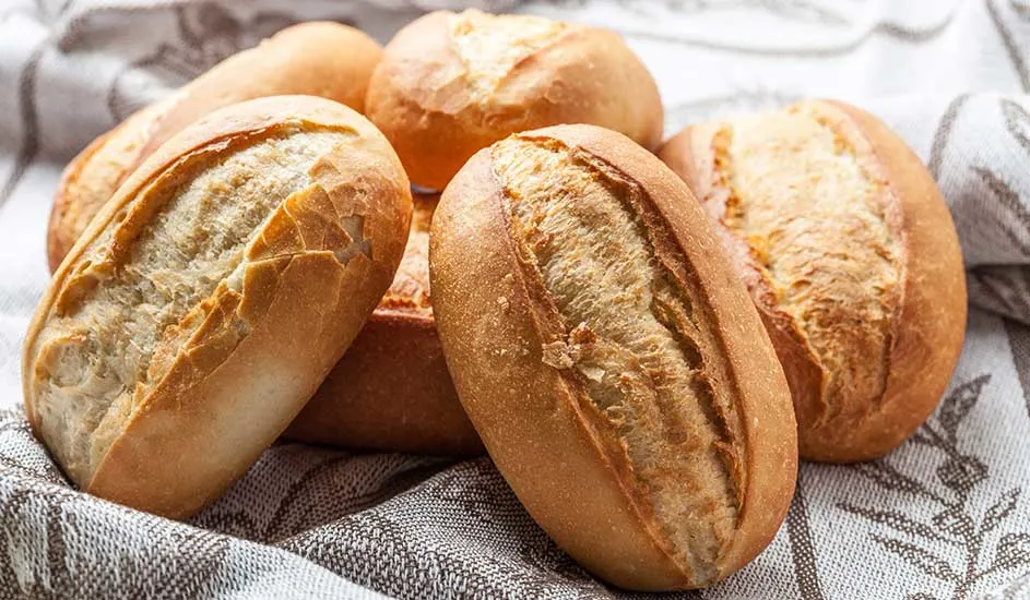 Zes knapperige witte pistoletjes liggen op een wit met grijs keukendoek. Het merk van het brood is niet zichtbaar op de afbeelding.