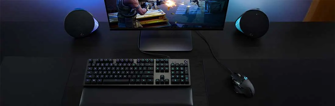 Donkere gaming opstelling met groot scherm, RGB toetsenbord, muis en krachtige luidsprekers, terwijl een actiespel vol explosies wordt gespeeld.