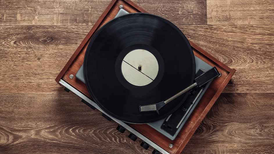 Een platenspeler met een zwarte vinylplaat erop, geplaatst op een bruine houten ondergrond.
