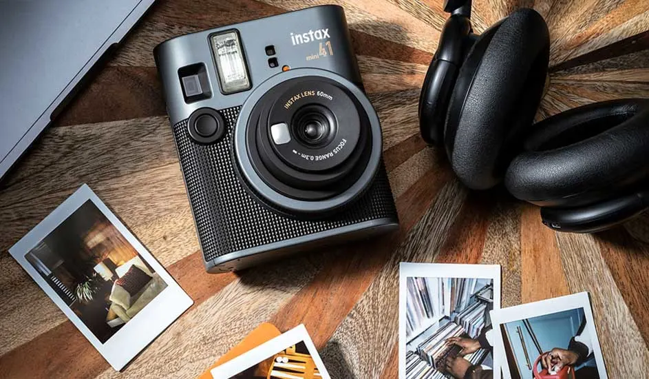 Een zwarte Instax-camera en een hoofdtelefoon liggen op een houten tafel naast ontwikkelde polaroidfoto’s van dagelijkse momenten.