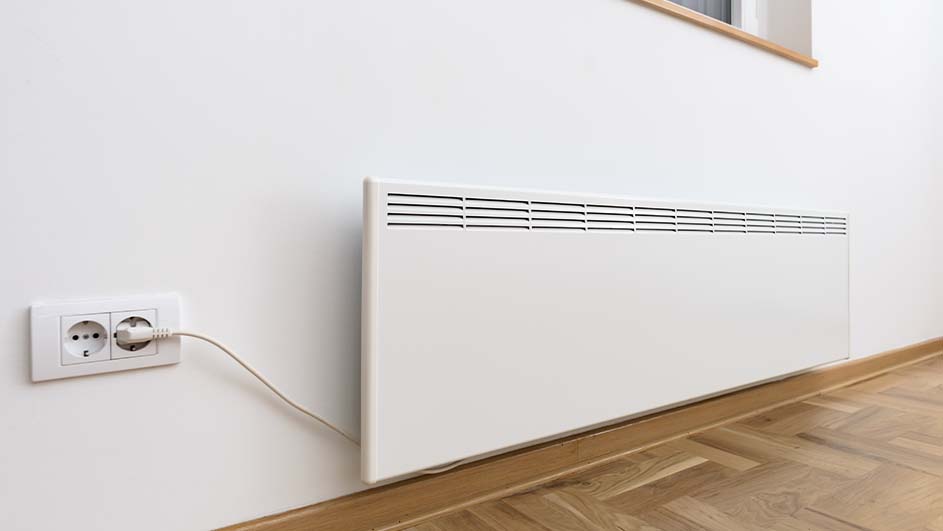 Een witte radiator hangt aan een witte muur boven een houten vloer. Een stekker zit in een stopcontact.