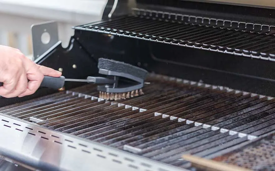Een hand reinigt zorgvuldig de roosters van een gasbarbecue met een borstel, klaar om hem proper en veilig te gebruiken.