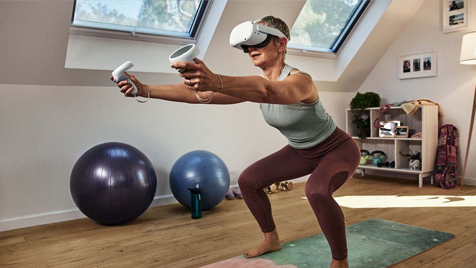 Vrouw met VR-bril en controllers, hurkend op een yoga mat. Achtergrond: sportballen, stellingkast en dakraam.