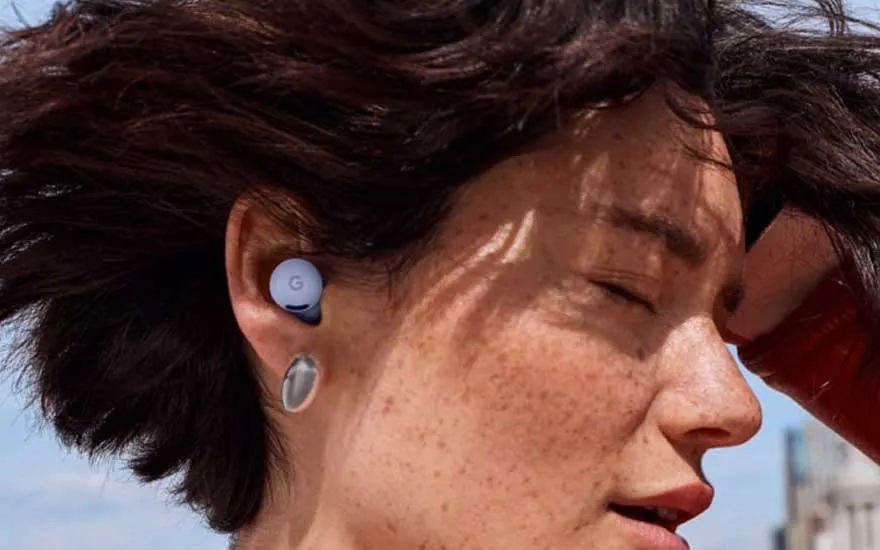 Close-up van een persoon met kort haar die Pixel Buds draagt, ogen gesloten, genietend van muziek in de buitenlucht.