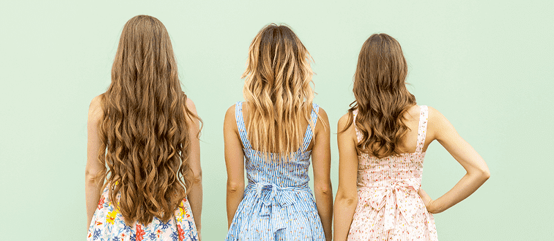 Drie vrouwen staan rug aan rug, gekleed in zomerjurken met bloemen- en streepmotieven tegen een lichtgroene achtergrond.