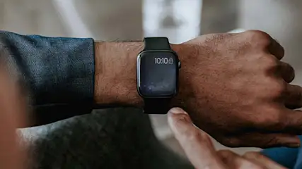 Een arm met een zwart horloge dat 10:10 aangeeft, een vinger wijst naar het scherm.